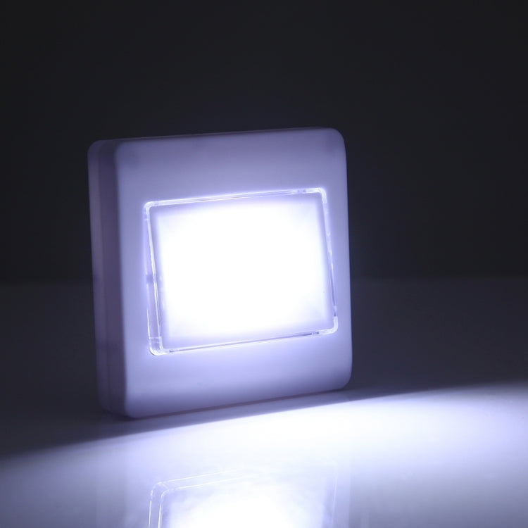 Square white night light lamp glowing brightly on a dark wall