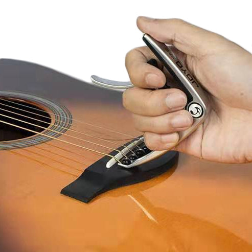 Black guitar capo in hand, spring clamp resting on guitar strings