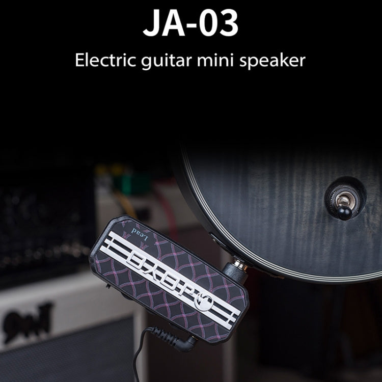 Mini guitar effects pedal with black patterned body placed near an electric amplifier.