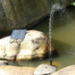 Solar water fountain pump spraying water stream from nozzle near pond rocks