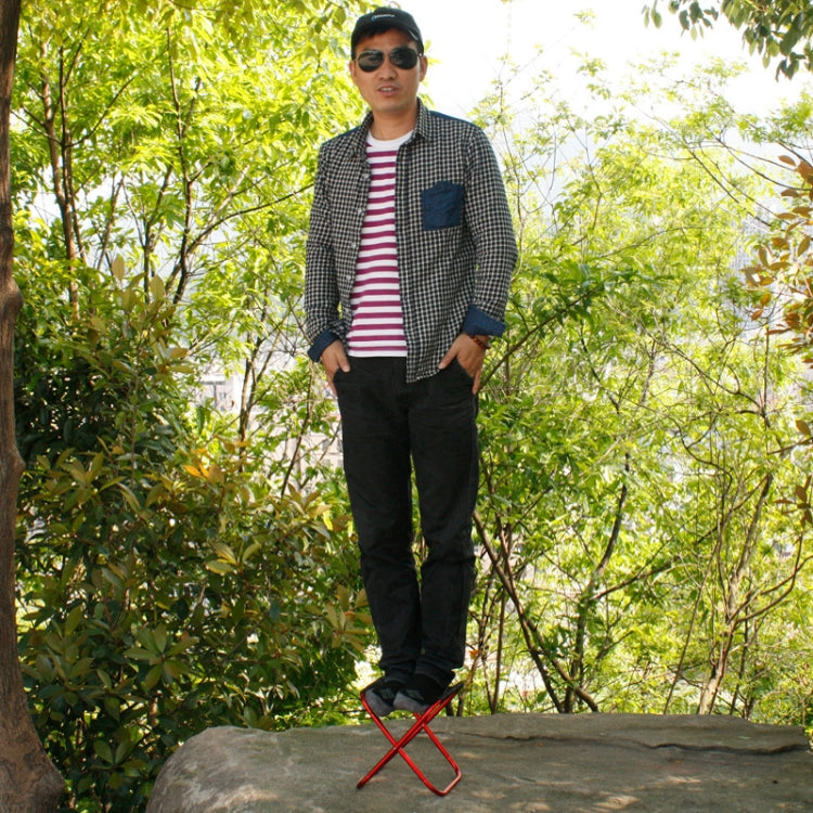 Outdoor portable folding stool with red frame and black fabric seat, used outdoors.