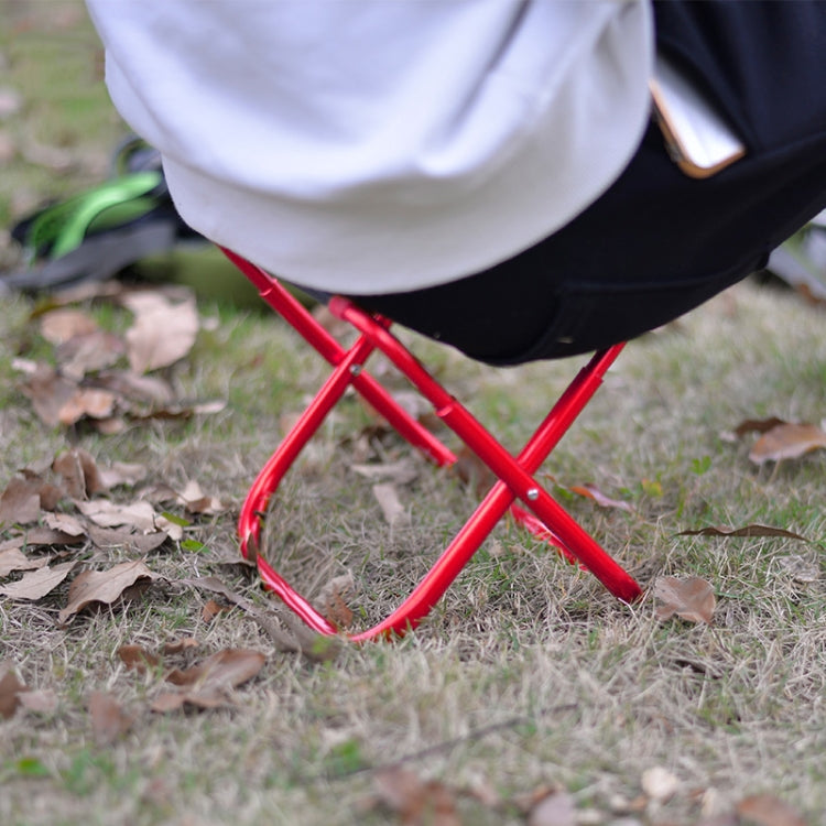 Red portable folding stool with black fabric seat and red metal legs, outdoor close-up.