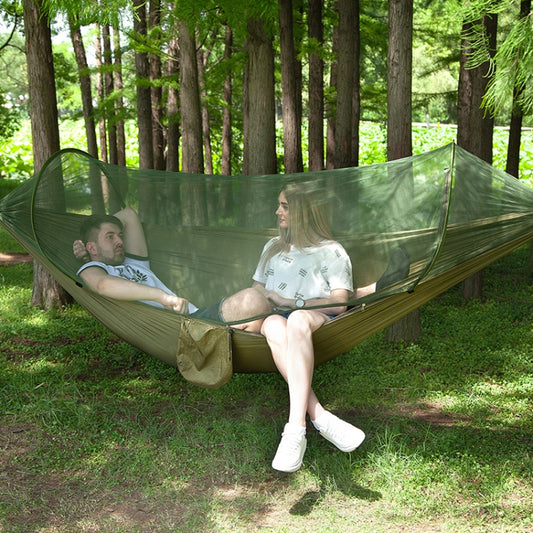 Green parachute hammock with mosquito net, two people relaxing outdoors
