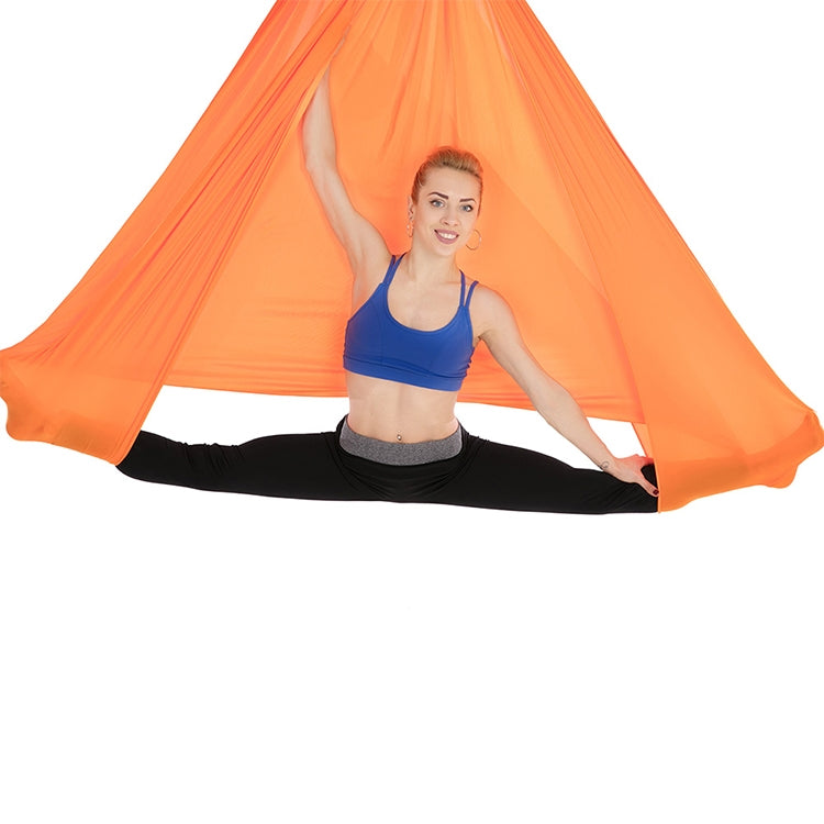 Orange aerial yoga hammock set with elastic ropes, person seated in a stretching pose