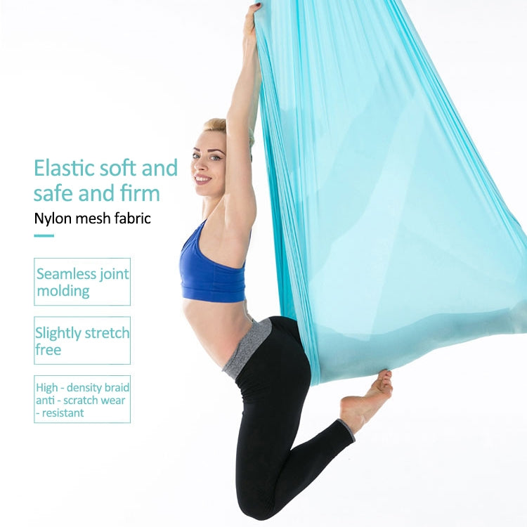 Light blue aerial yoga hammock set, person kneeling while holding elastic ropes overhead