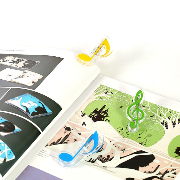 Multiple music note spring page clips in clear plastic holding open photo book pages