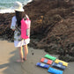 Pink waterproof dry bag with roll-top closure on a person near the shoreline.