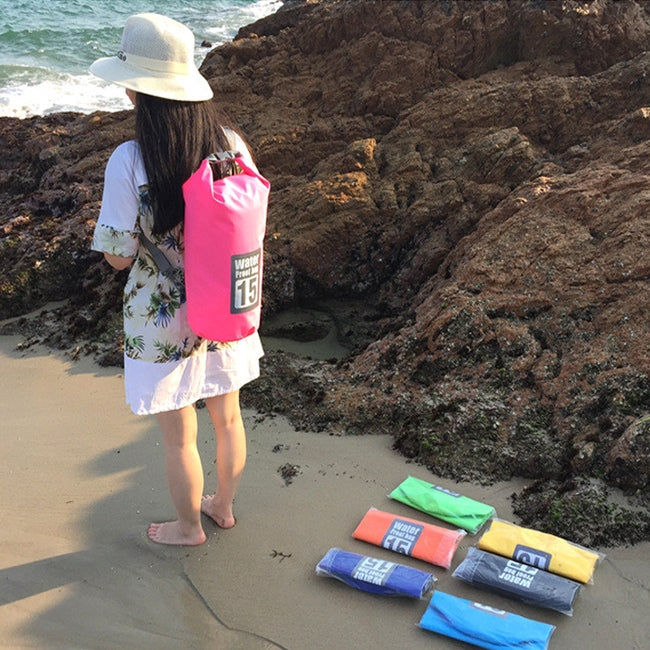 Pink waterproof dry bag with roll-top closure on a person near the shoreline.
