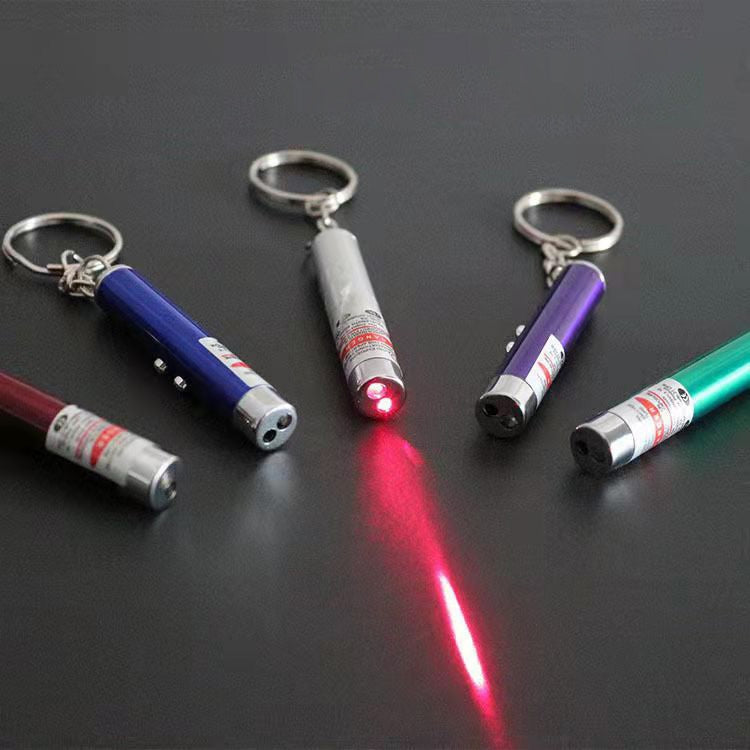 Multiple LED laser pen keychains on a dark surface with a red laser beam spot.