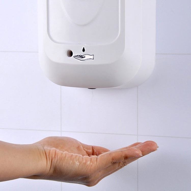 Hand under touchless liquid soap dispenser spout on a tiled wall