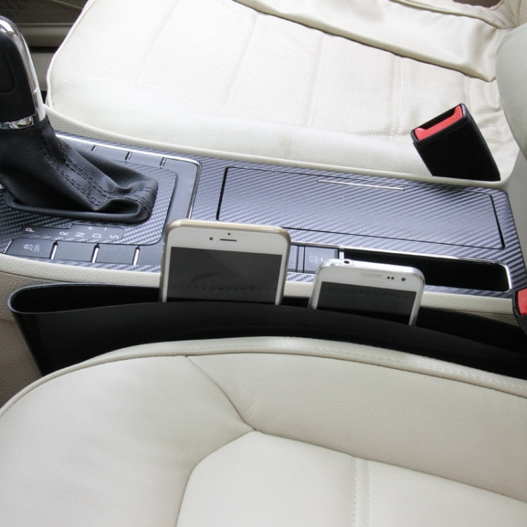 Black car seat gap organizer installed between seats, holding phones and small items