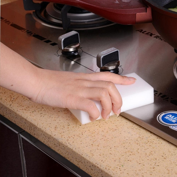 Hand using a white cleaning sponge block on a stove surface.