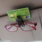 Black sunglass clip mounted on car visor holding a business card