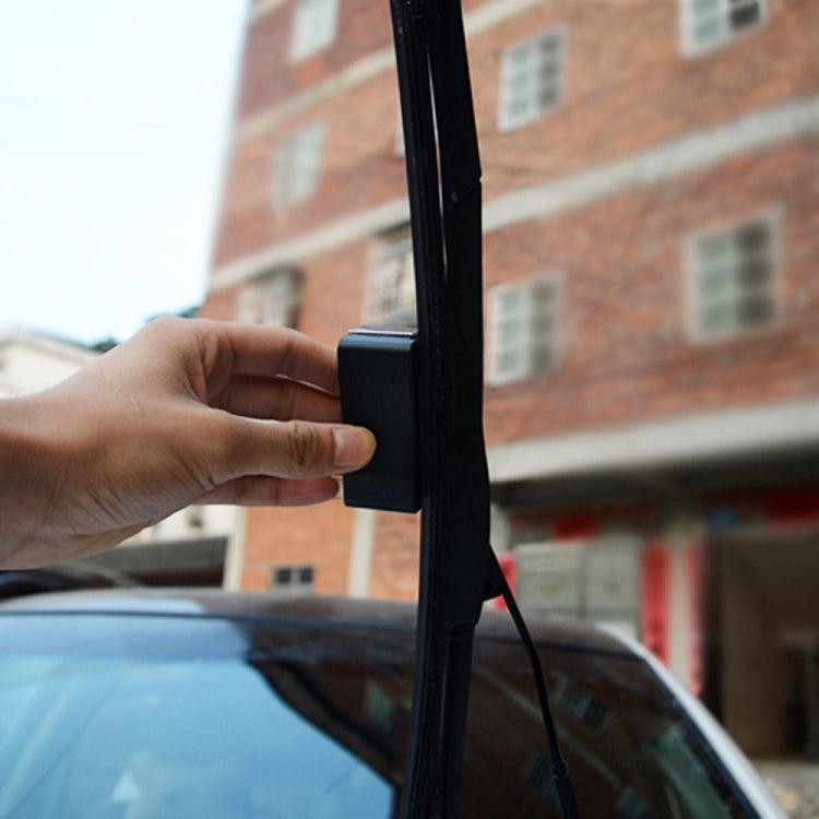 Hand holding a black wiper blade restorer tool against a car wiper
