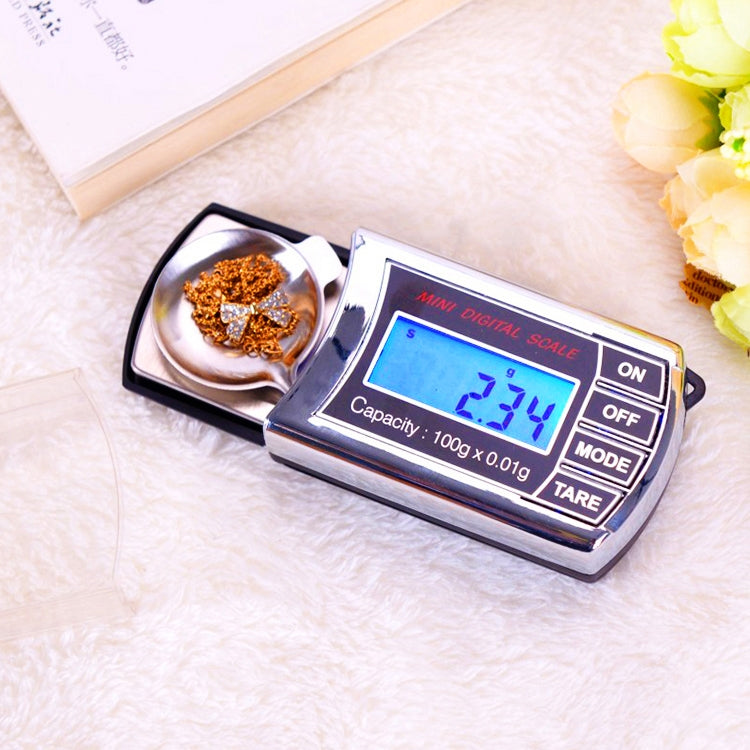 Mini digital scale on surface, LCD display lit and weighing tray with metal flakes