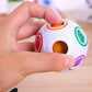 Hand holding white magic ball puzzle cube with orange ring and colored windows