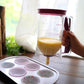 Batter dispenser cup pouring pale batter into cupcake liners with pink lid