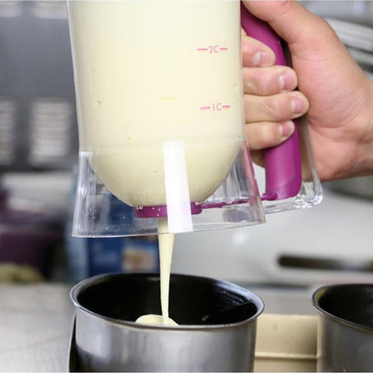 Hand holding batter dispenser cup as batter pours from the pink spout into a pan