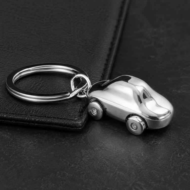 Car-shaped metal key chain with split ring and small wheels on dark surface