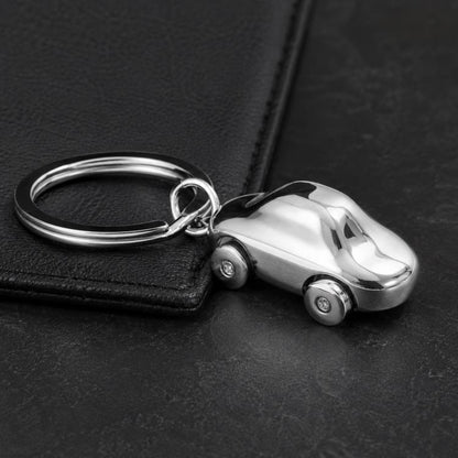 Car-shaped metal key chain with split ring and small wheels on dark surface