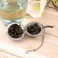 Large stainless steel tea infuser ball filled with dried tea leaves, with chain