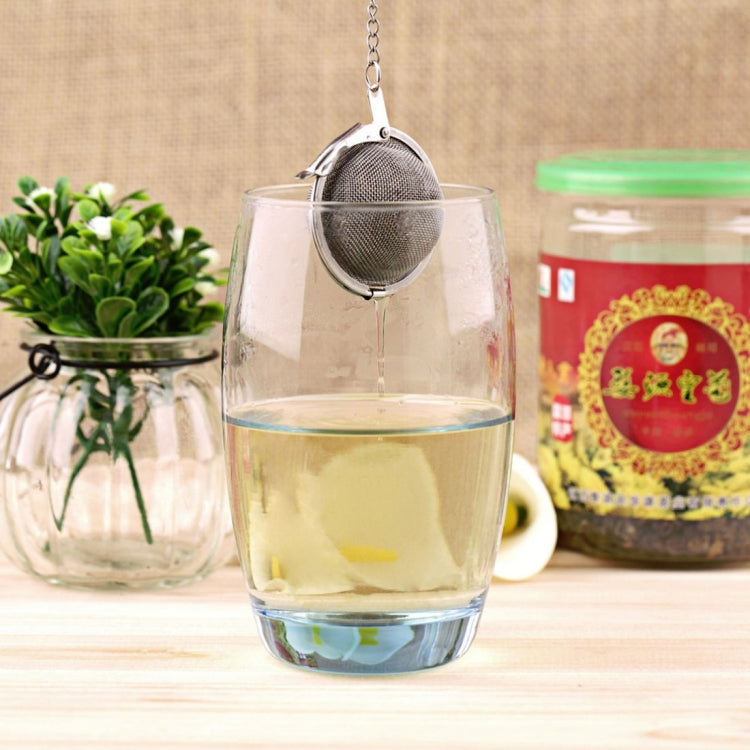 Large stainless steel mesh tea infuser ball hanging inside a glass mug