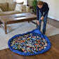 Round blue kids toy storage bag with toy pieces inside on a living room floor