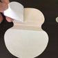 Adhesive underarm pad held in hand, showing backing layer, white