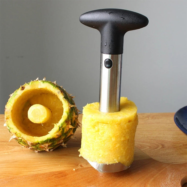 Pineapple corer slicer with black handle and silver metal tube, over halved pineapple