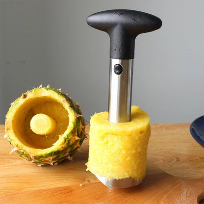 Pineapple corer slicer with black handle and silver metal tube, over halved pineapple