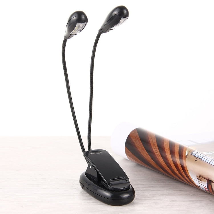 Dual-arm clip-on LED reading light with two heads mounted on desk beside a book