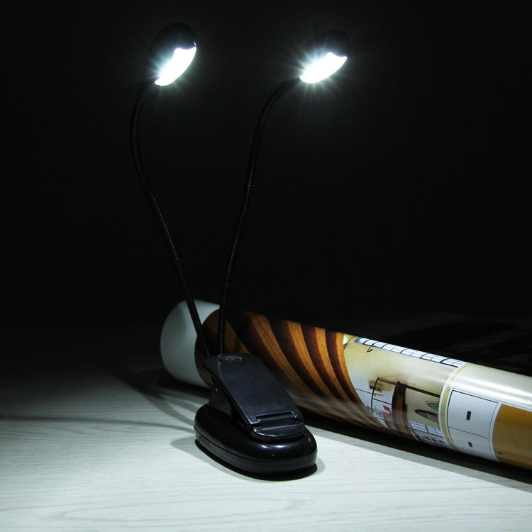 Dual-arm clip-on LED reading light switched on, shining onto a book on a tabletop
