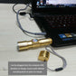 Gold LED flashlight connected by USB cable for charging next to a laptop