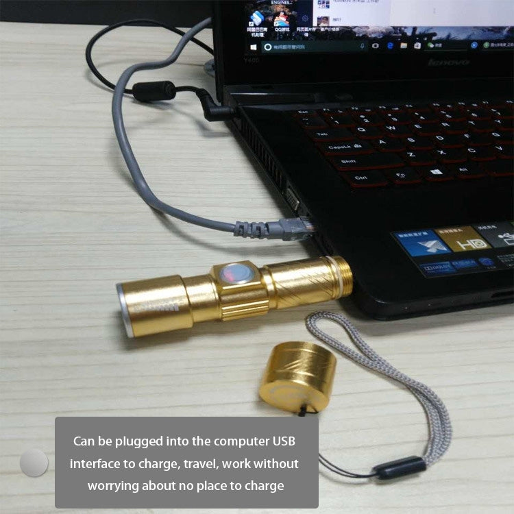 Gold LED flashlight connected by USB cable for charging next to a laptop
