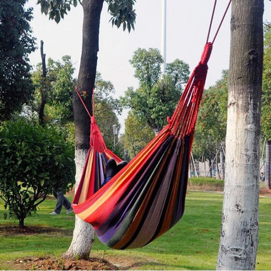 Multicolor striped canvas hammock with fringed suspension ropes, spread on both ends