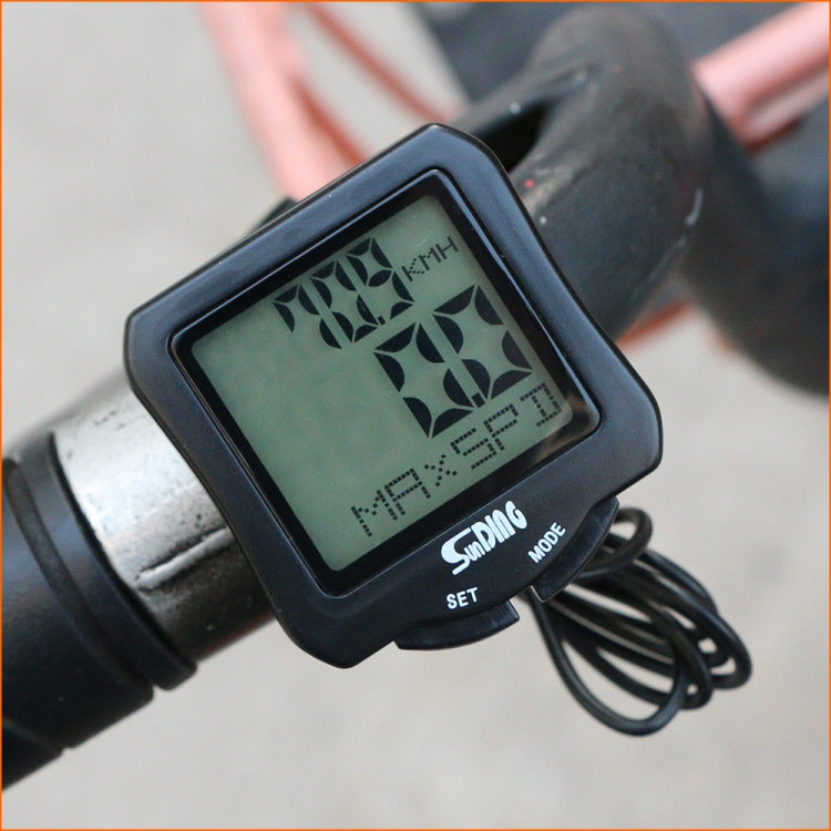 Black bicycle computer with green LCD on handlebar clamp, showing speed/clock icons