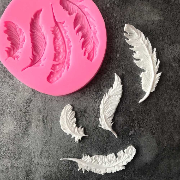 Pink round silicone mold with feather-shaped cavities and three white feather molds