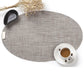 Oval PVC dining table mat in linen beige fabric, with cup and saucer on it