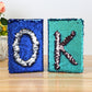 Lake blue sequin flip notebook with dark K letter, shown beside another sequin notebook