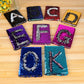 Assorted sequin flip letter notebooks on table, including lake blue K design