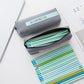 Open gray pencil case with mint front label, zipper top and pencils inside