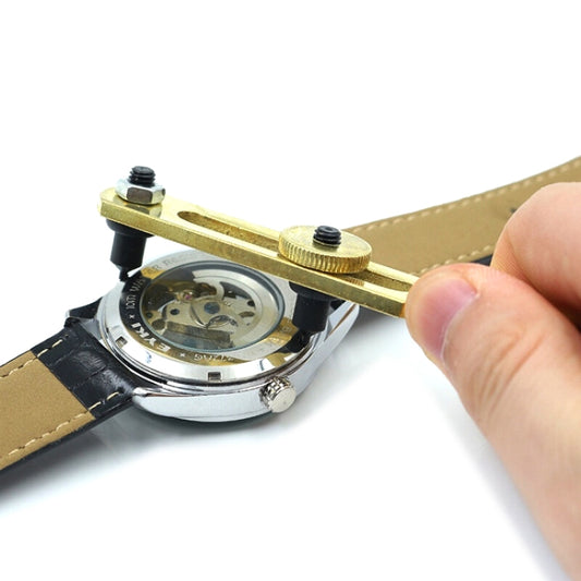Two-jaw watch back cover opener wrench with brass handle and black grips, held by hand