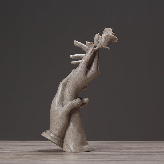 Abstract light-gray sculpted hands reaching upward with a small rose on top.