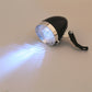 Black retro bicycle LED headlight with silver rim, beam shining forward