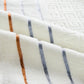Close-up of light beige towel fabric with blue and orange stripe bands and textured pattern