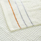 Close-up of light beige cotton towel with orange and blue vertical stripes and embossed weave