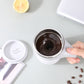 Electric white stirring cup with dark coffee inside and lid placed aside.