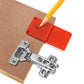 Orange hinge positioner template with silver hinge kit and pencil tip over wood