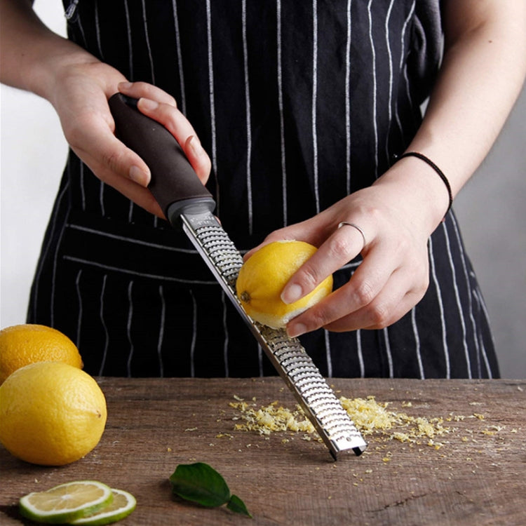 Stainless steel grater with black handle grating lemon on a wooden board.