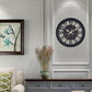 Round black quartz wall clock mounted on wall with ornate roman numerals and gears